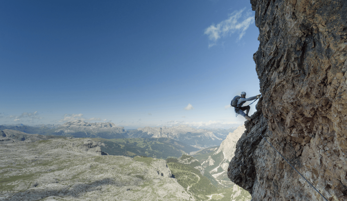 Person rock climbing on side of mountain with landscape and horizon in the background